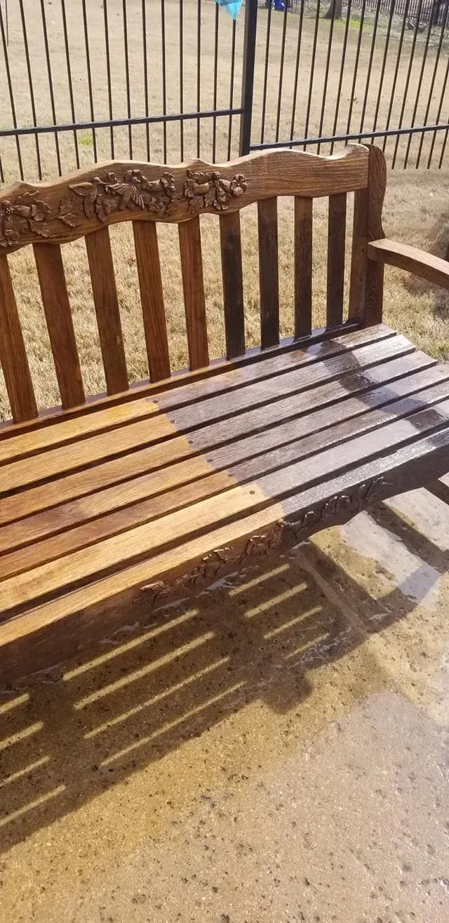 A wooden garden bench showing a clear color difference from staining progress, half light, half dark, on a patio.