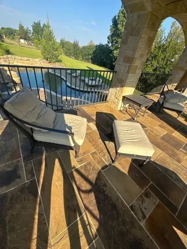 A lounge chair and ottoman on a stone patio overlooking a pool and grassy hillside.