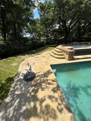 A stone pool deck and tiered steps leading to a spa, featuring a pressure washer surface cleaner on the patio.