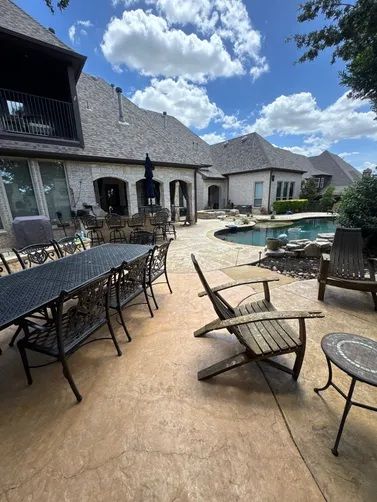 A backyard patio with outdoor dining furniture and lounge chairs overlooking a swimming pool on a sunny day.