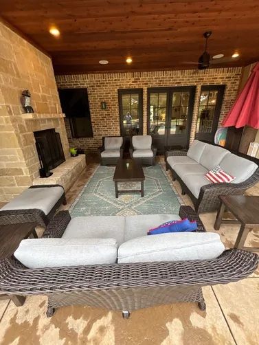 Outdoor patio with gray wicker seating, a stone fireplace, and a blue area rug under a covered wood ceiling.