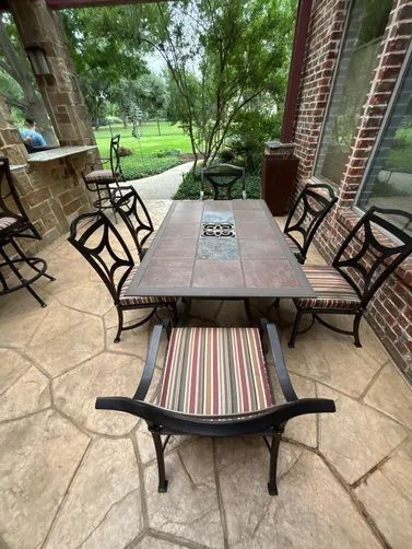 A patio table with chairs, striped cushions, and a stone-look tabletop on a stone floor with a brick wall in the background.