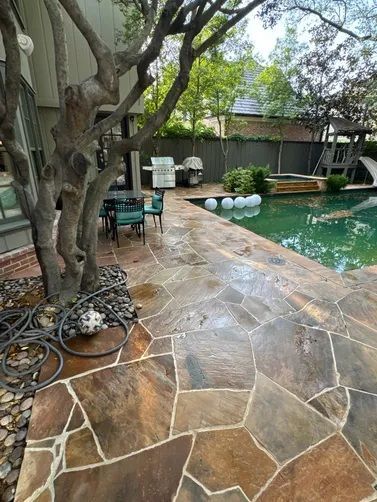 A flagstone patio featuring a large tree, a bistro set, a swimming pool with floating lights, and a wooden play structure.