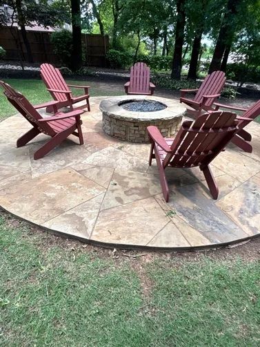 Five red Adirondack chairs arranged in a circle around a stone fire pit on a circular patio in a backyard.