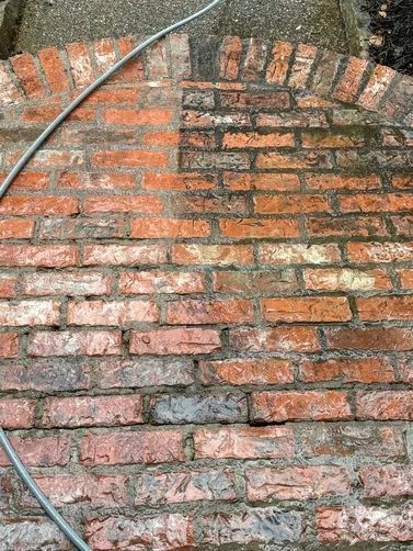 A brick patio shows a clean, bright left side contrasted with the dark, moss-covered right side during power washing.