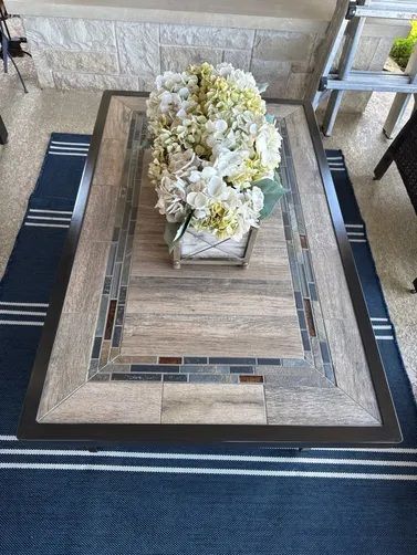 A rectangular outdoor coffee table with a tiled surface and mosaic border, topped with a white floral centerpiece.