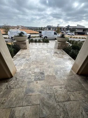 Stone patio with two large planters, leading to a driveway with two white service vans under a cloudy sky.