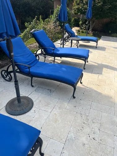 Three blue lounge chairs with umbrellas arranged on a light-colored stone patio in a sunny outdoor setting.