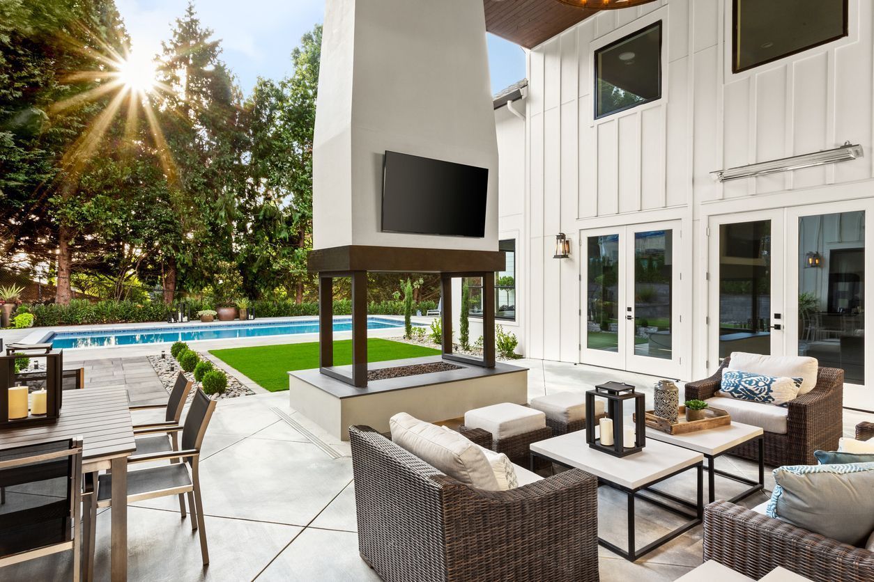 Modern patio with wicker seating, outdoor fireplace, pool, and bright white house exterior