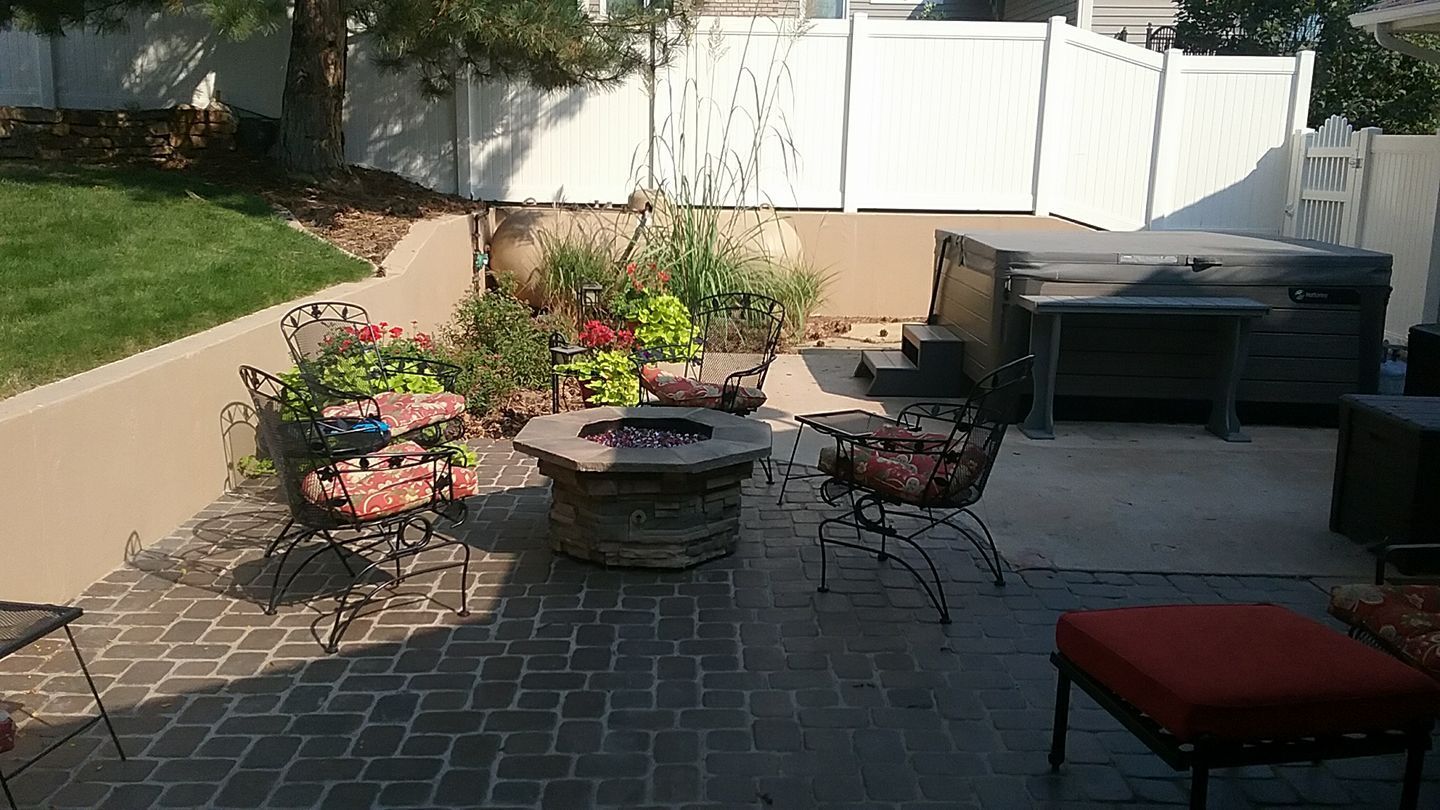 Backyard patio with fire pit, hot tub, and seating, enclosed by a white fence.