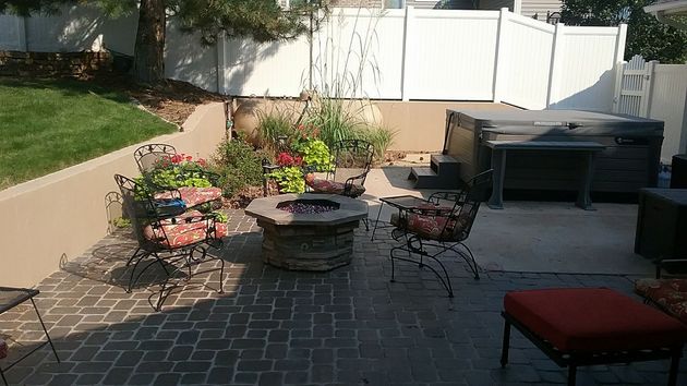 Backyard patio with fire pit, hot tub, and seating, enclosed by a white fence.