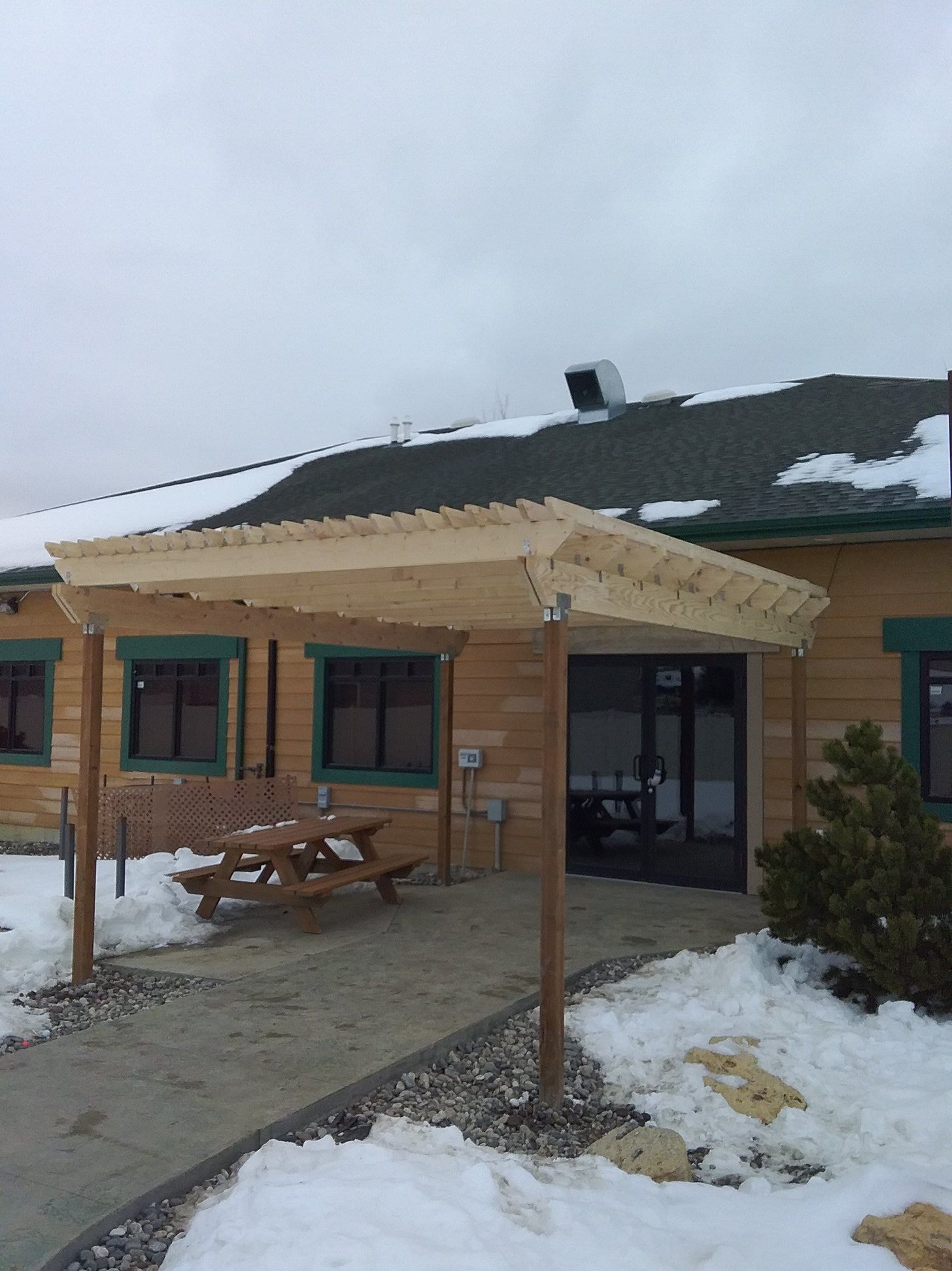 Pergola over a picnic table in front of a building with snow.