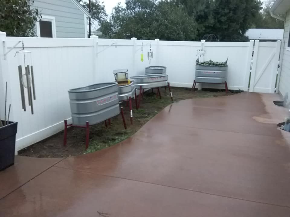 Backyard with metal trough planters and white fence, brown concrete patio.