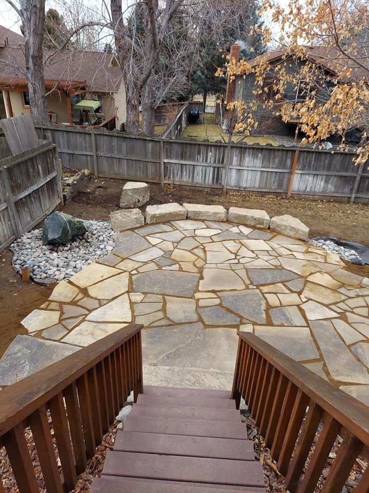Stone patio with wooden stairs in a backyard setting.