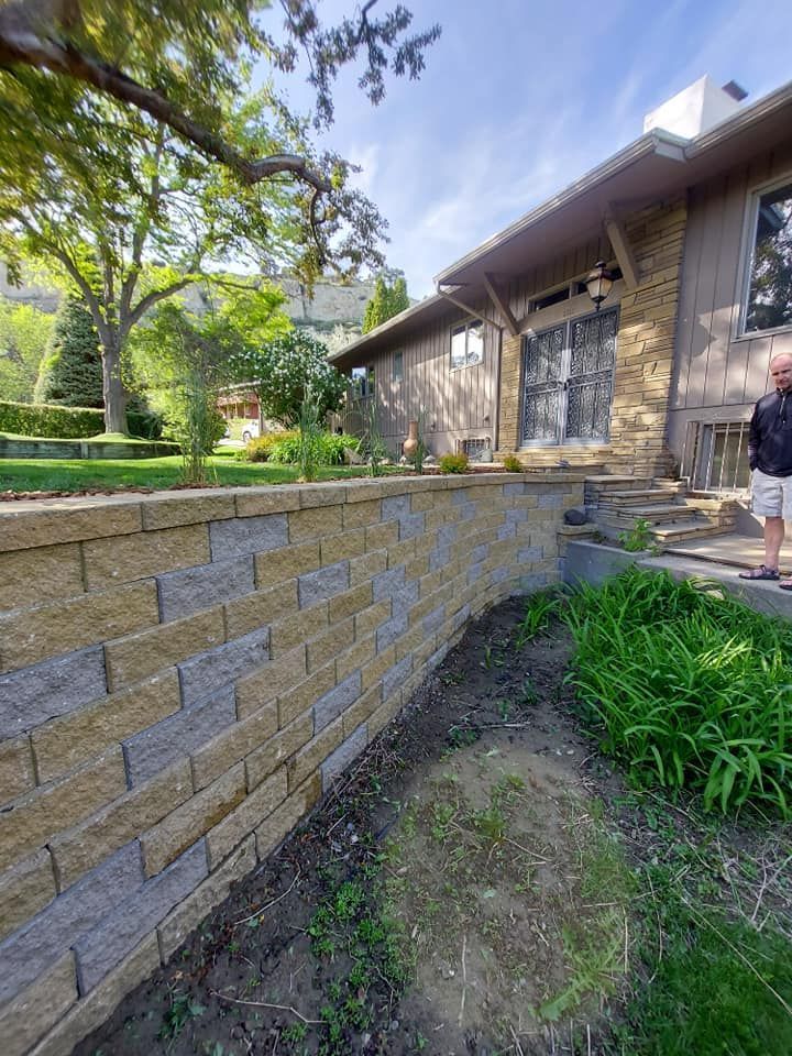 Stone retaining wall beside a house; a person stands on a porch. Sunny day.
