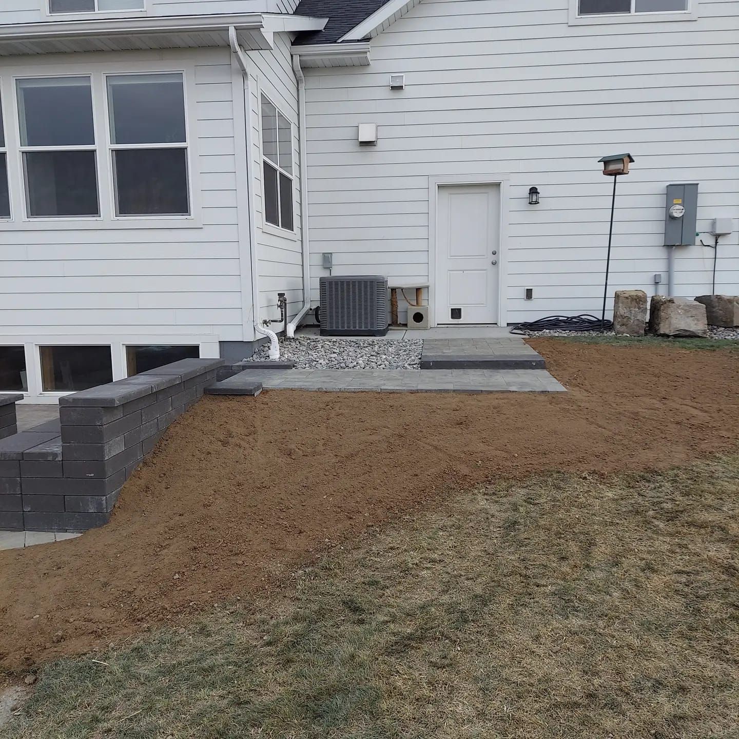 Back of a white house with a patio, retaining wall, and lawn.