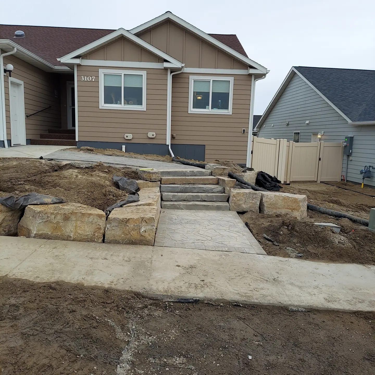 Tan house with concrete steps and retaining wall. Pathway from the sidewalk to the front door.