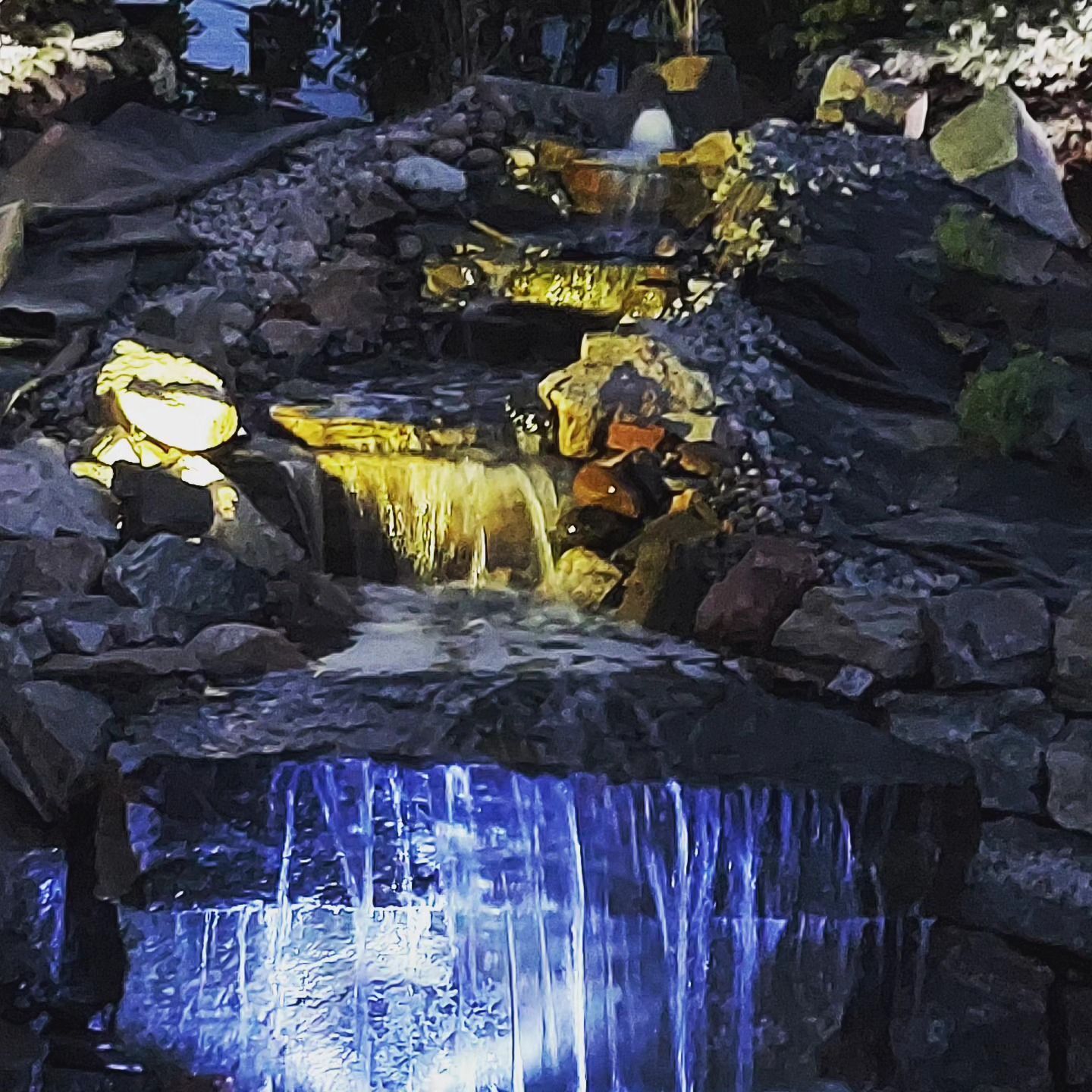 Water cascading down a rock waterfall, illuminated with blue and yellow lights.