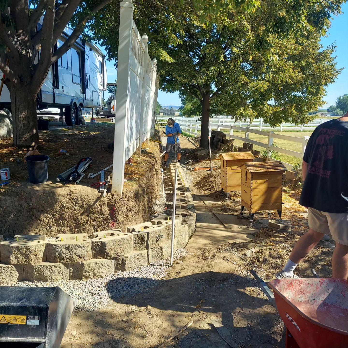 Construction site with retaining wall being built. Two people working; one with wheelbarrow.