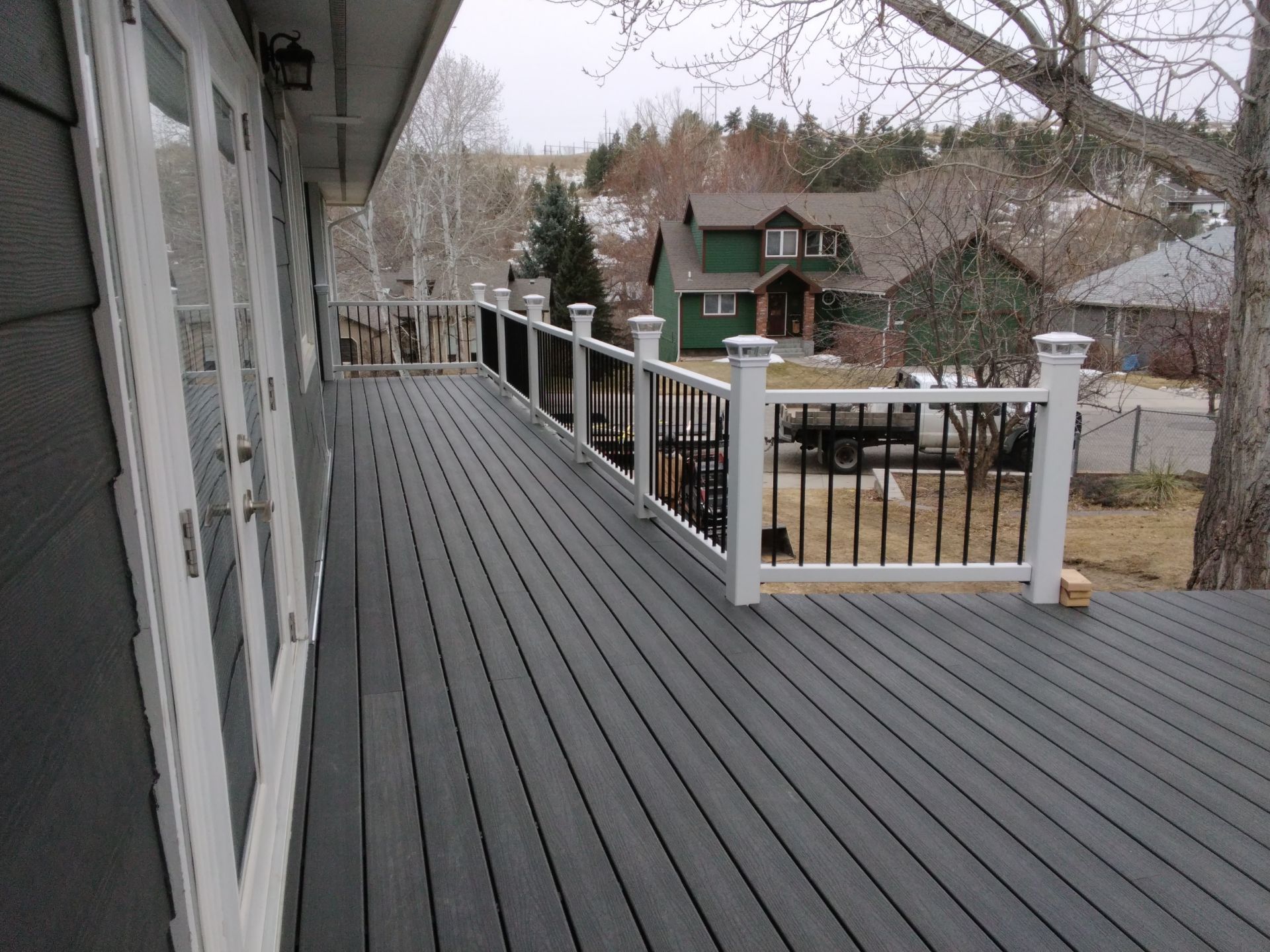 Gray composite deck with white railing, overlooking a neighborhood with houses and trees.