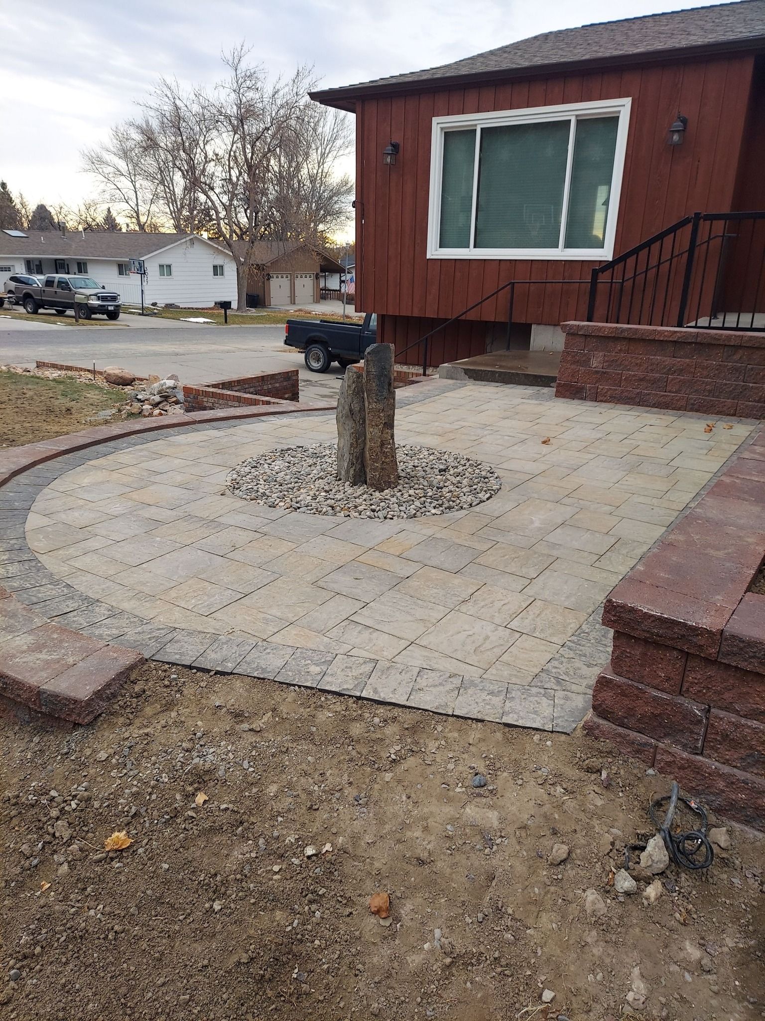 Circular paved patio with fountain feature; adjacent red brick walls and house with dark siding.