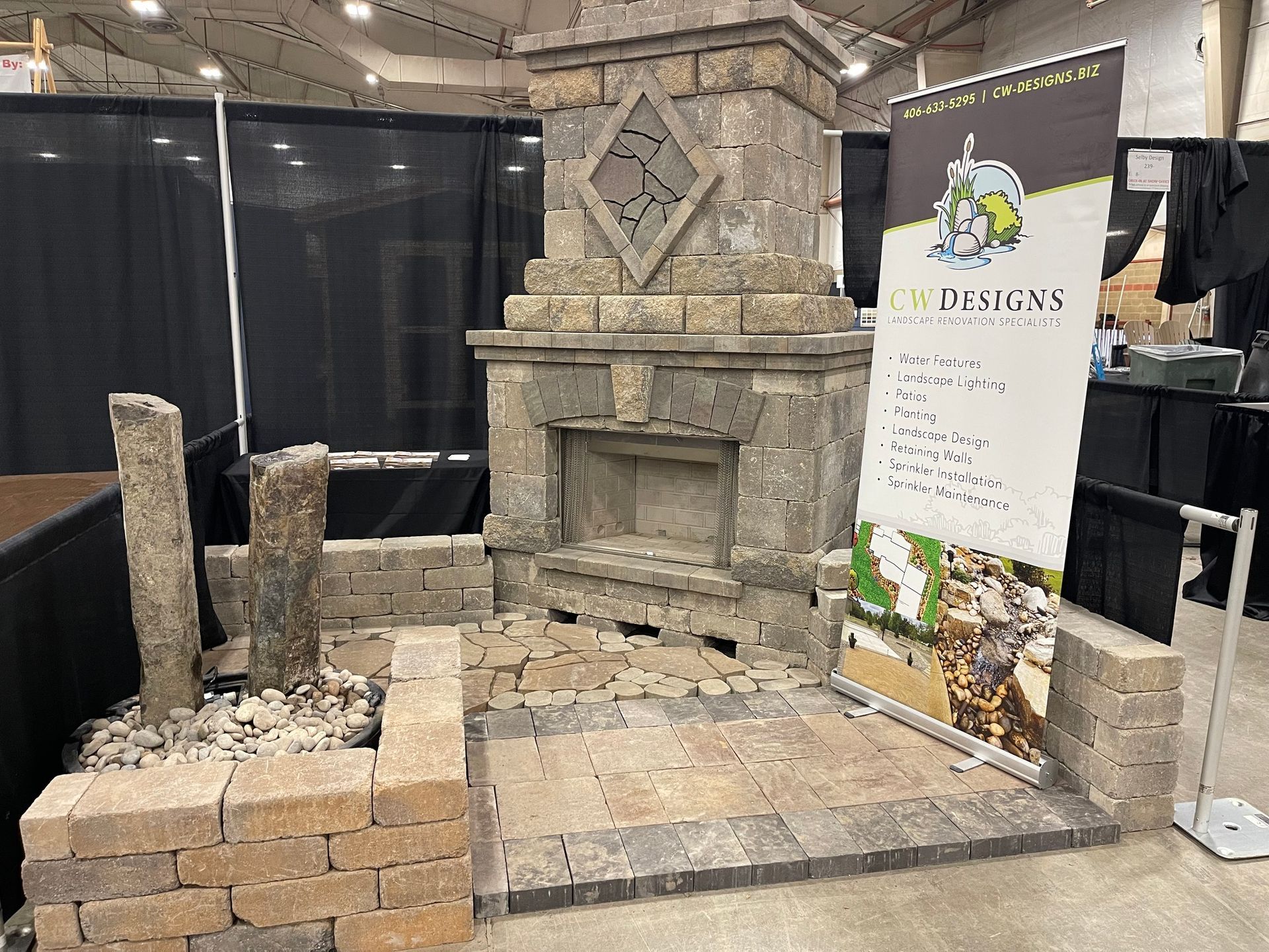 Stone fireplace display with pavers and a business banner at a trade show.