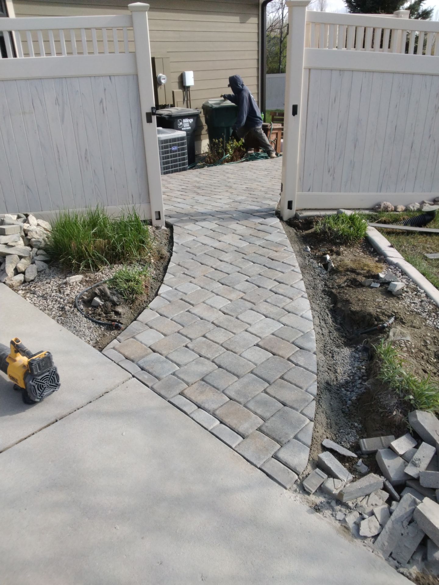 Brick pathway leading through a white fence. A person works in the background.