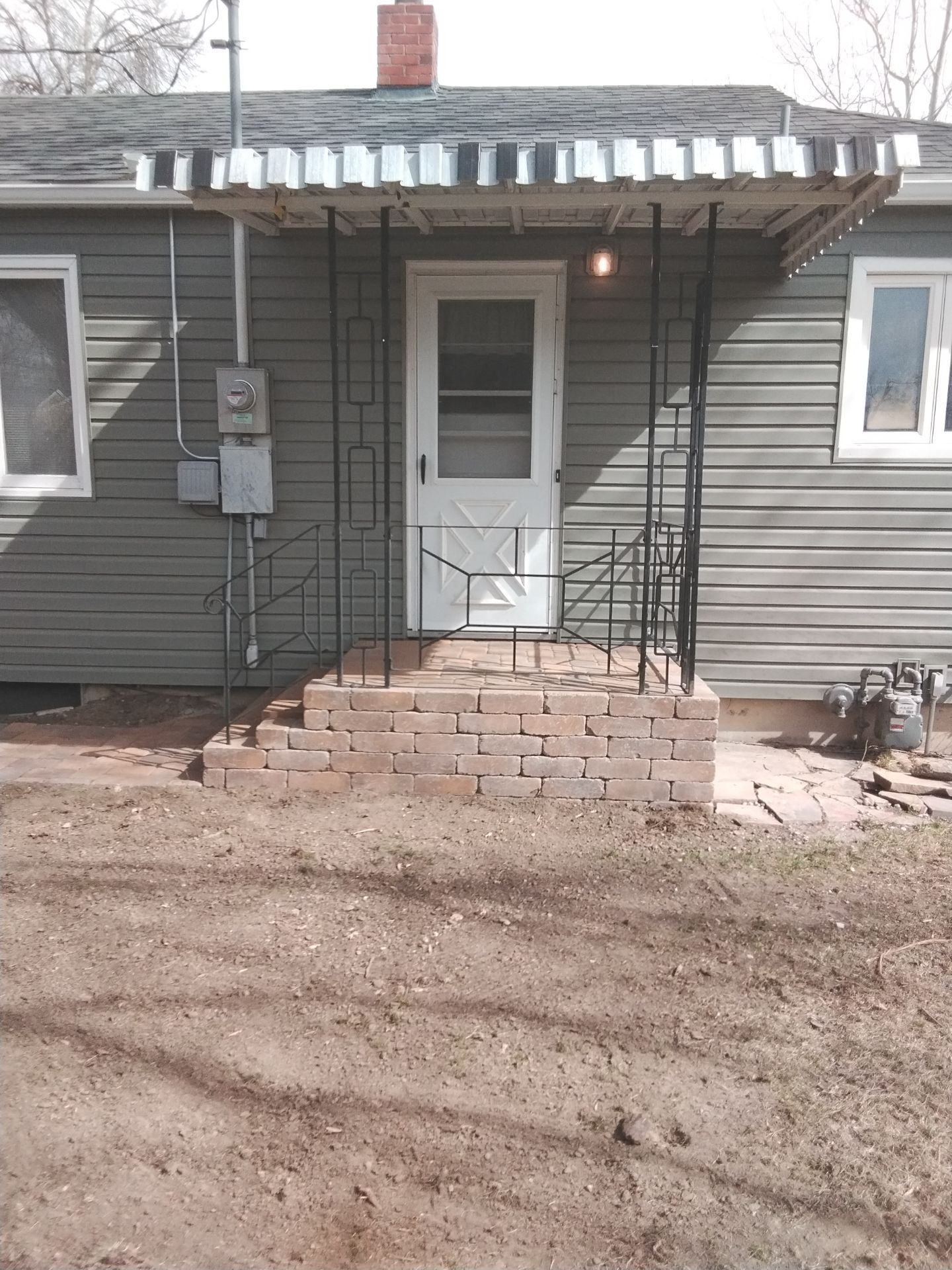 Green house with white door, metal awning, brick steps, and wrought iron handrails.