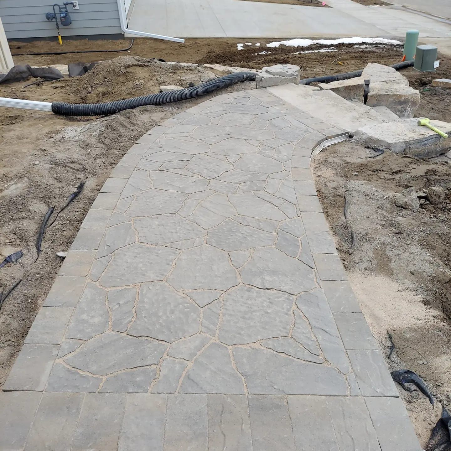 Gray stone pathway under construction with surrounding dirt and construction materials.