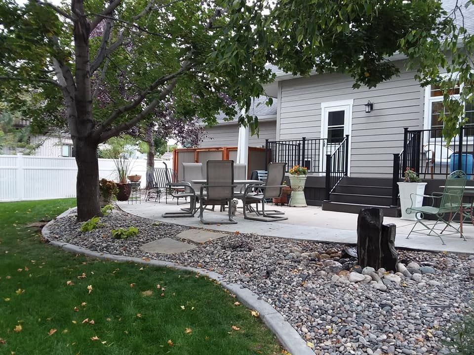 Backyard patio with seating, landscaping, and a water feature next to a house under a tree.