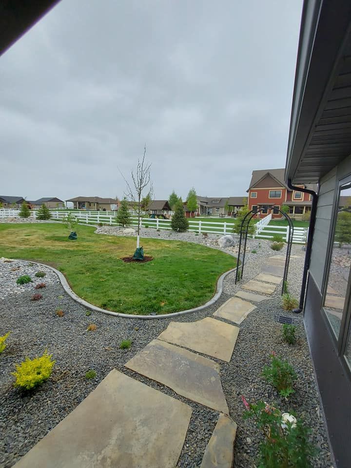 Backyard with stone path, green lawn, gravel border, white fence, and cloudy sky.