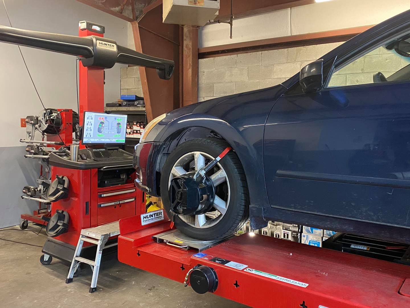 A blue car on an alignment rack at an auto repair shop; the machine is red and black.
