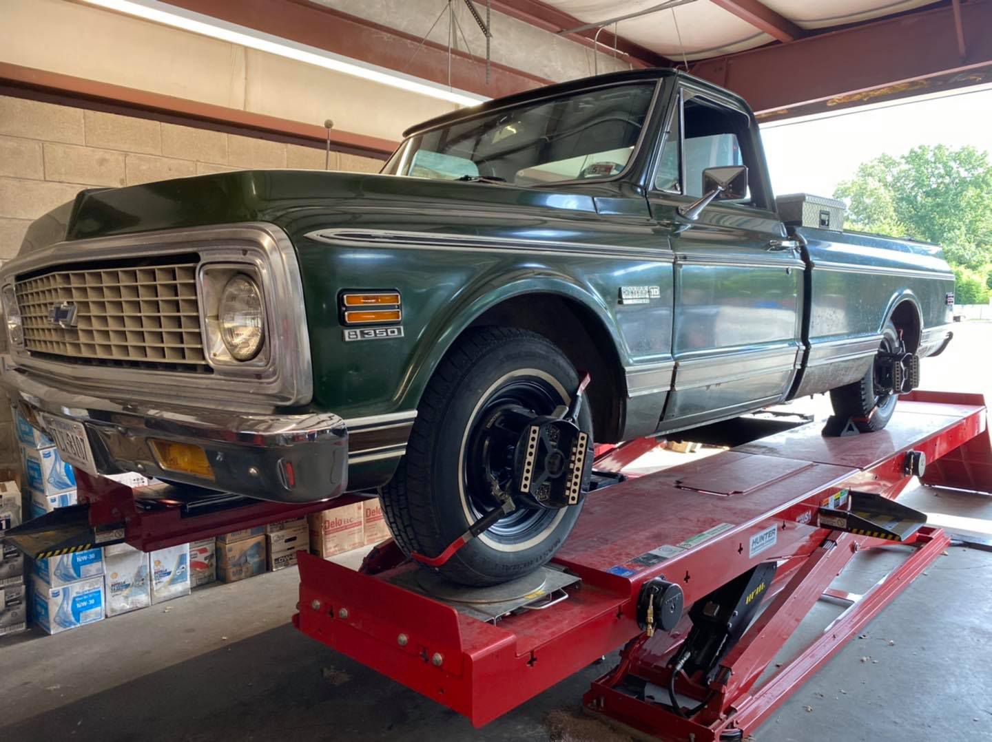Green vintage Chevy truck on a red car lift being aligned in a shop.