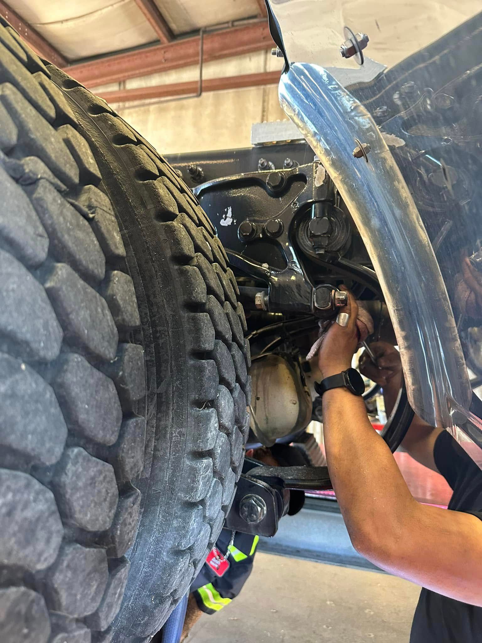 Mechanic working on a truck near a large tire. Hands visible, reaching. Interior setting.