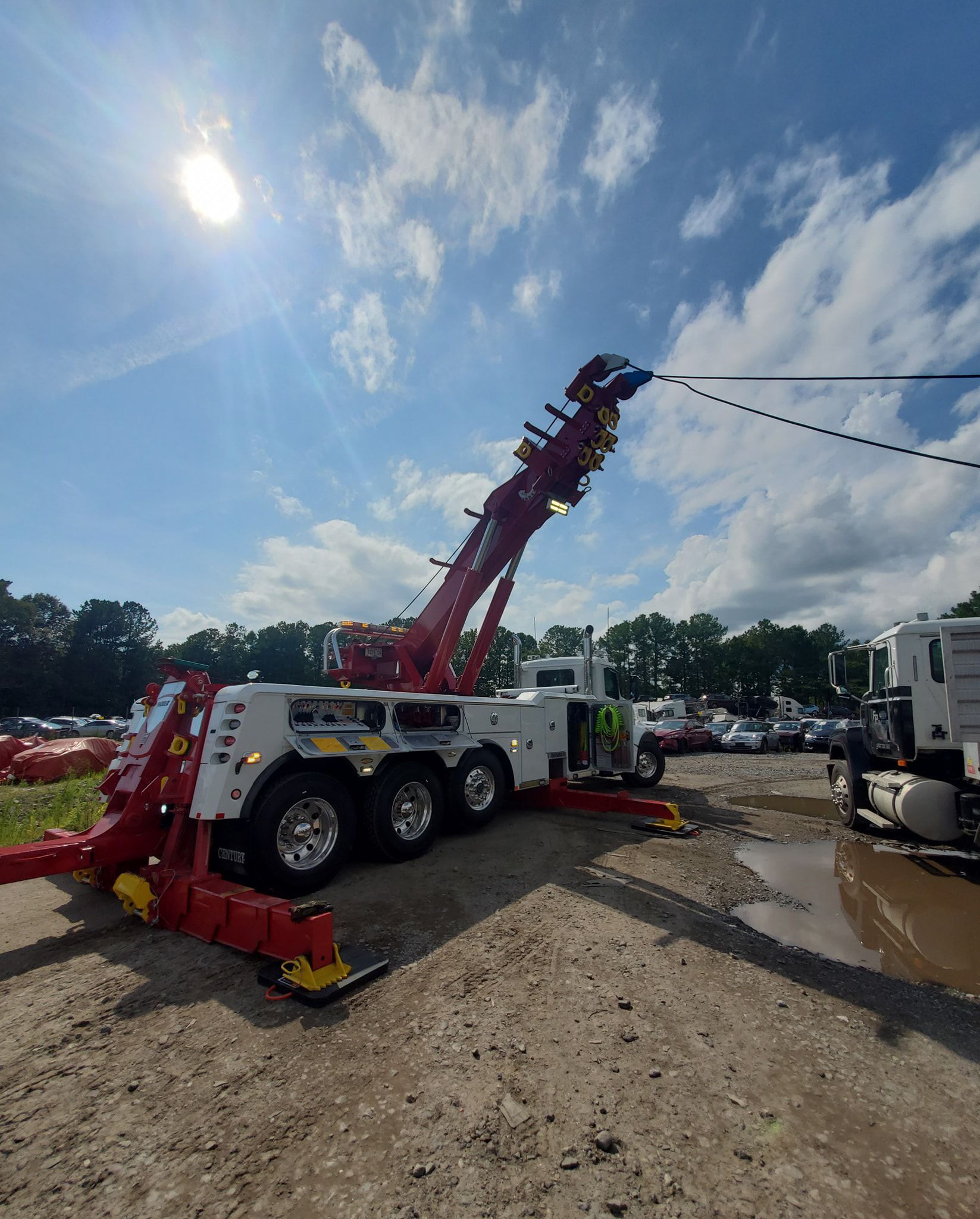 A large, red and white tow truck with its boom extended, against a cloudy sky.