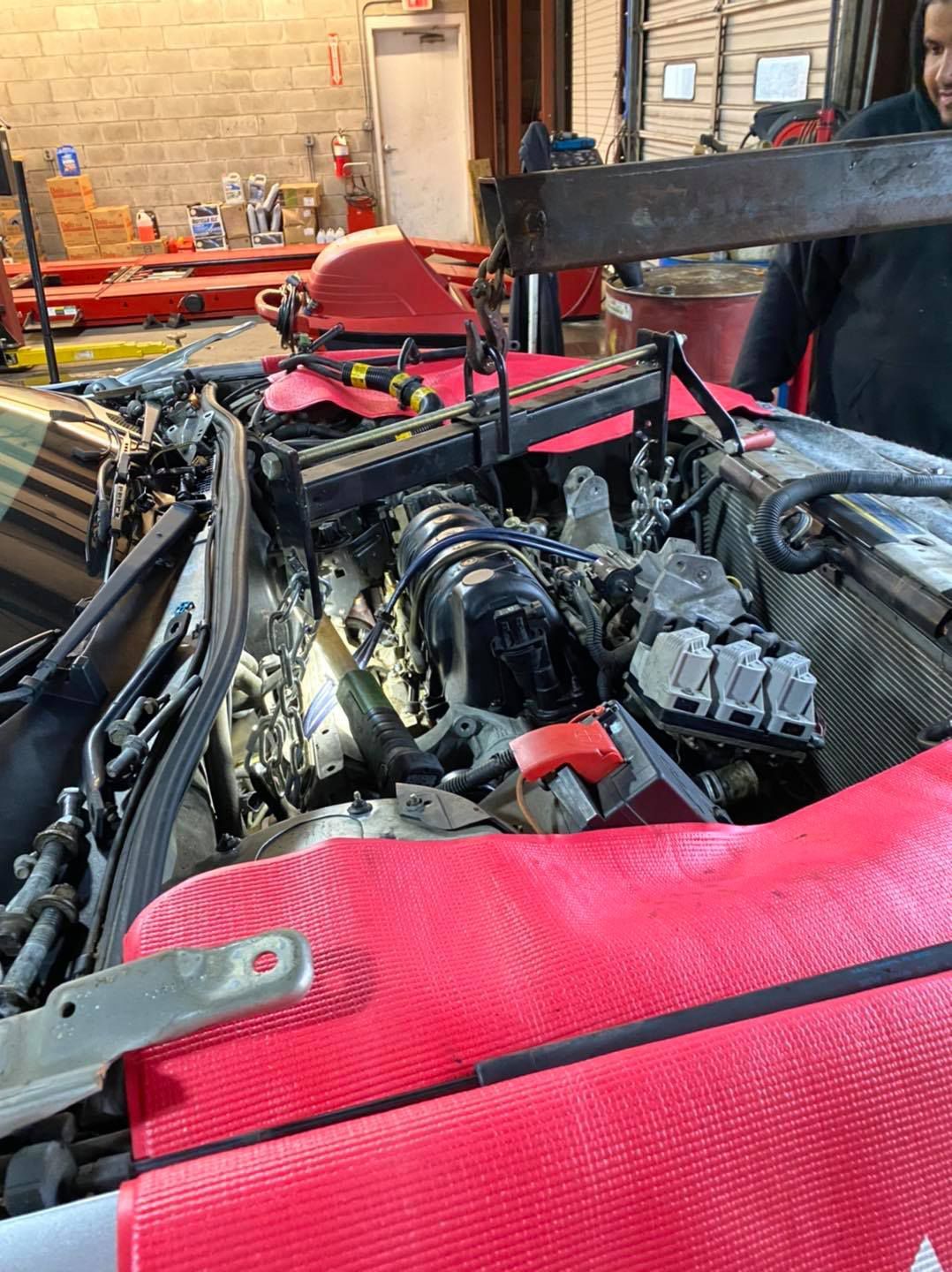 Engine being removed from a car in a repair shop. A worker stands nearby.