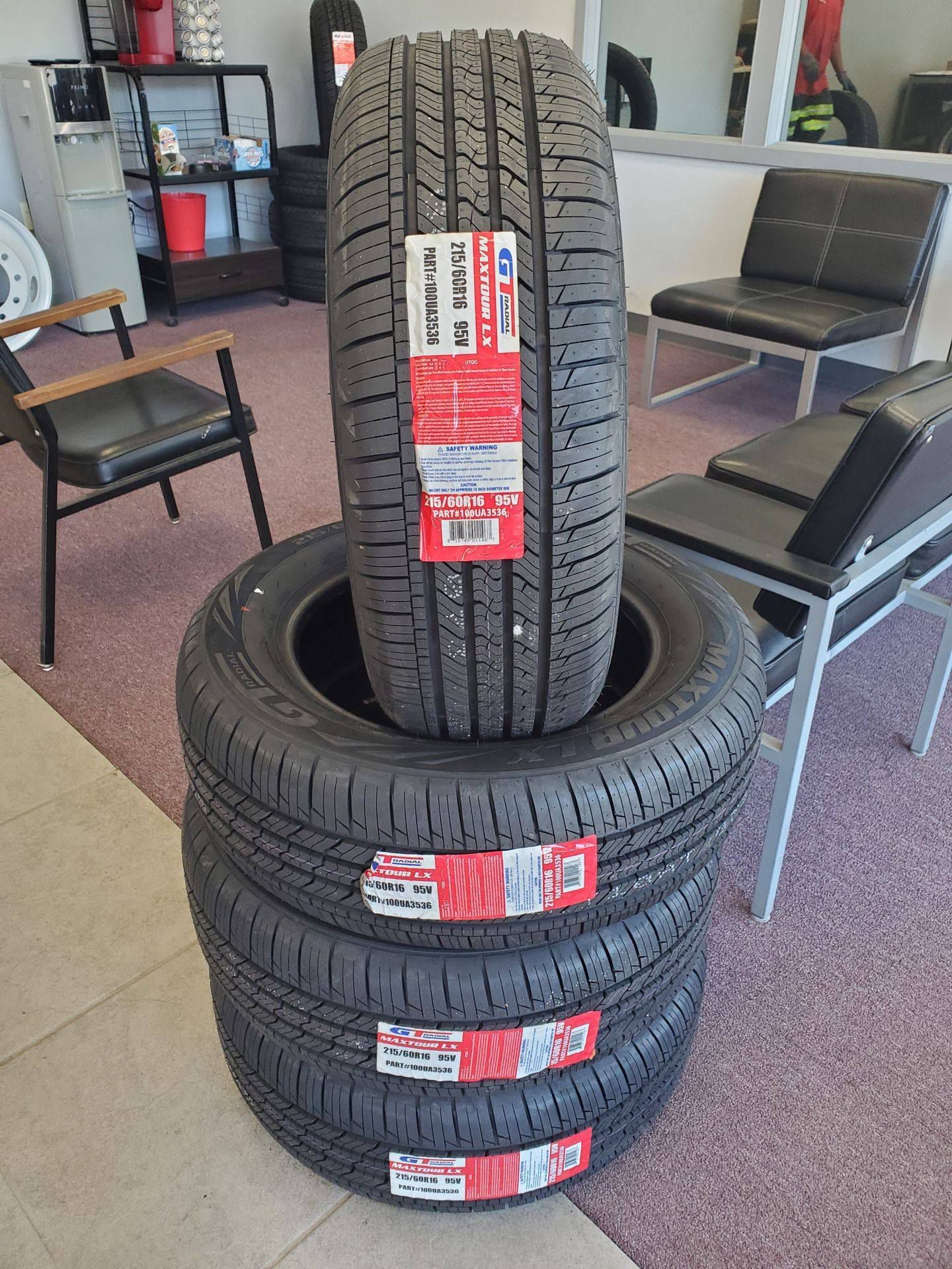 Four new black tires stacked, one upright, with red and white labels, inside a shop.