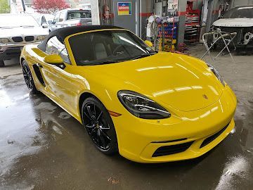 A bright yellow Porsche convertible parked in a car repair shop.