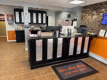 Interior view of the Lux Auto Body front office, featuring a black reception desk with metal panels and a branded rug.