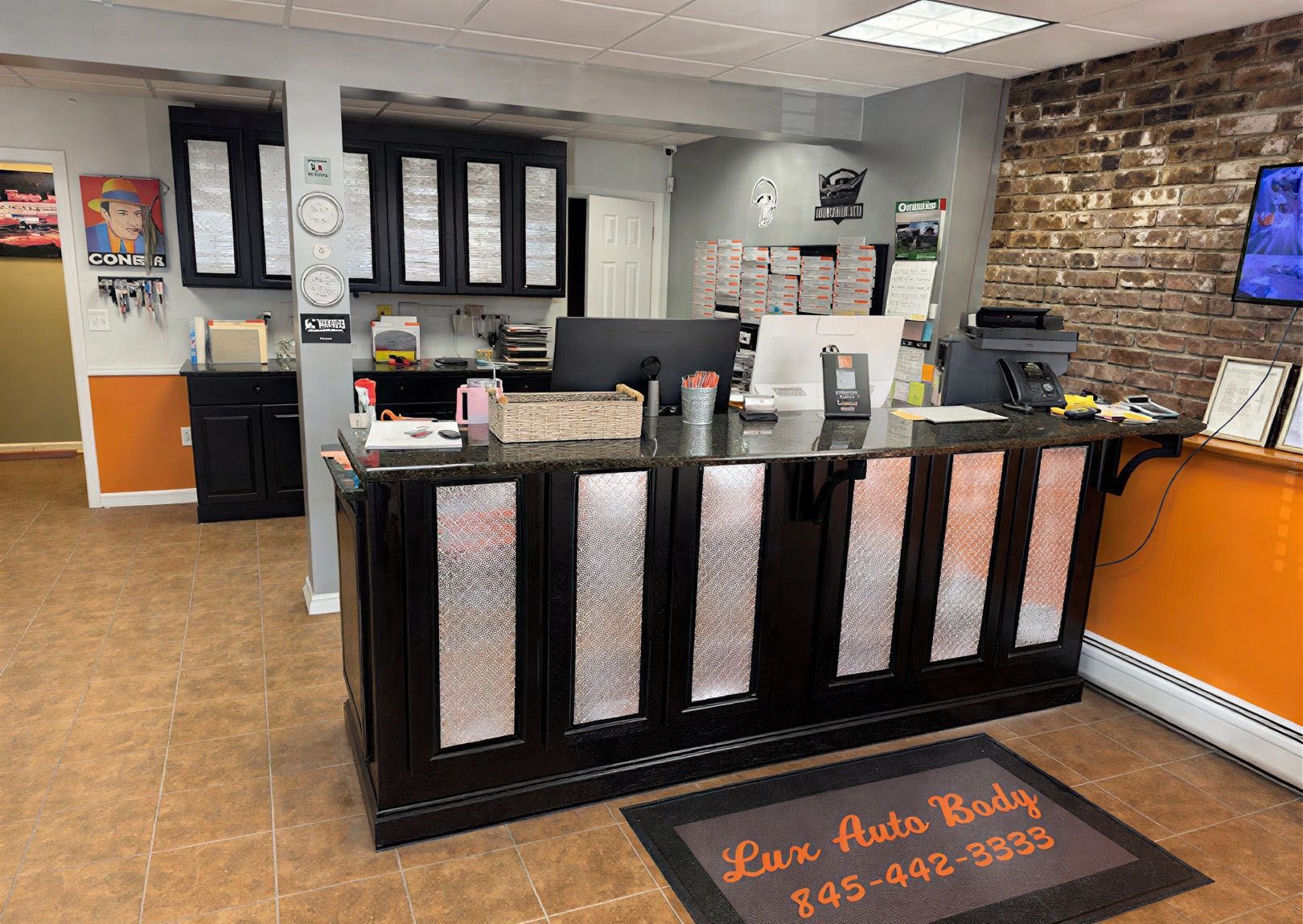 A reception desk with a black counter and metallic diamond-plate panels, set in an office with brick and orange walls.
