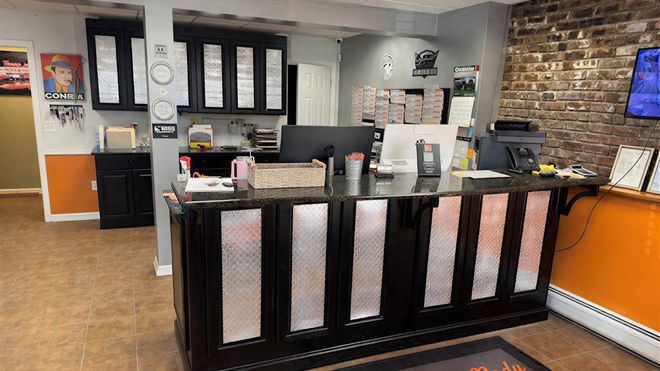 A reception desk with a black counter and metallic diamond-plate panels, set in an office with brick and orange walls.