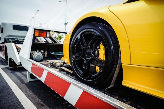A bright yellow sports car is secured onto the flatbed of a white tow truck.