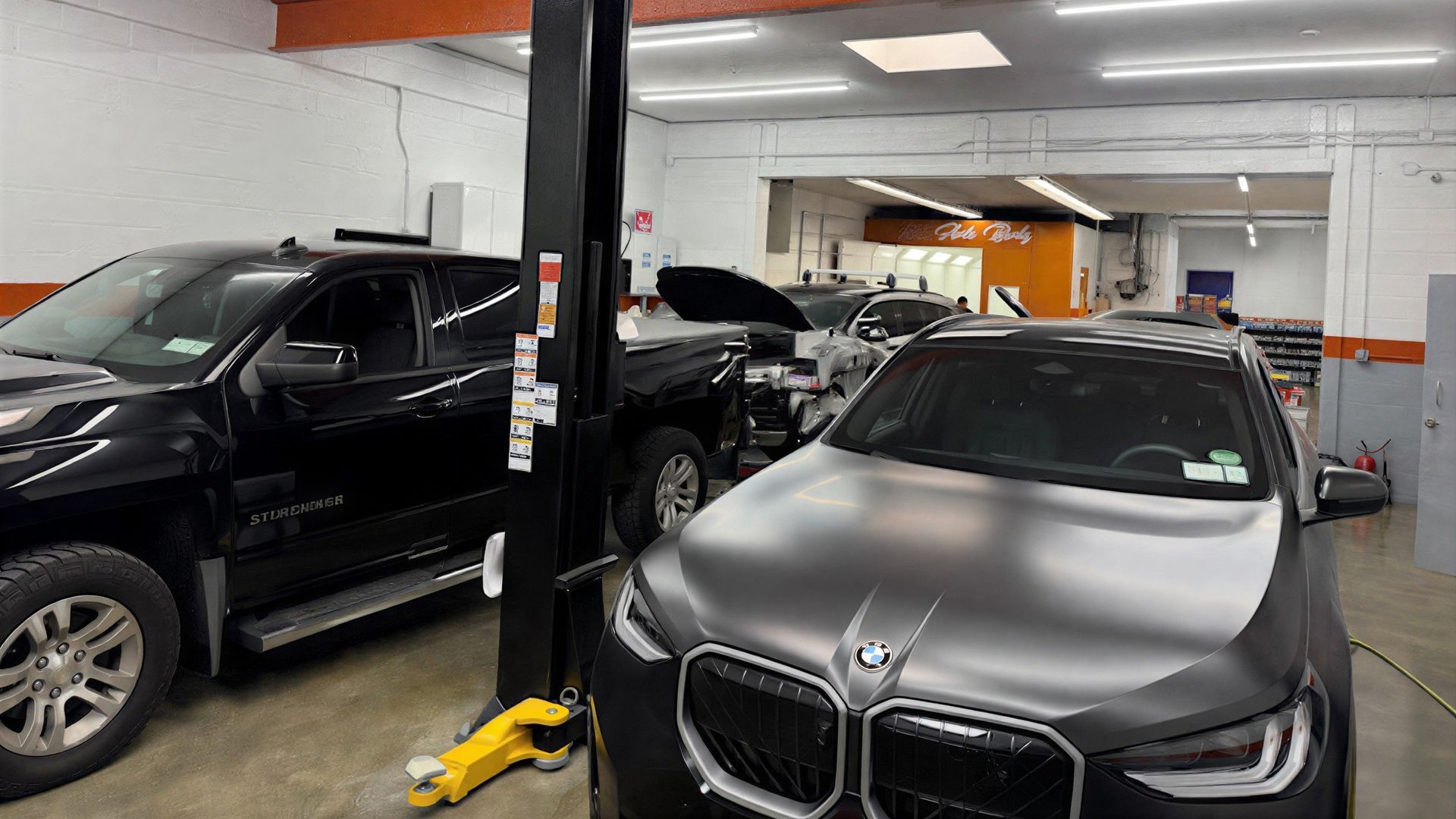 A black truck and a matte-finish BMW parked inside a well-lit automotive repair garage.