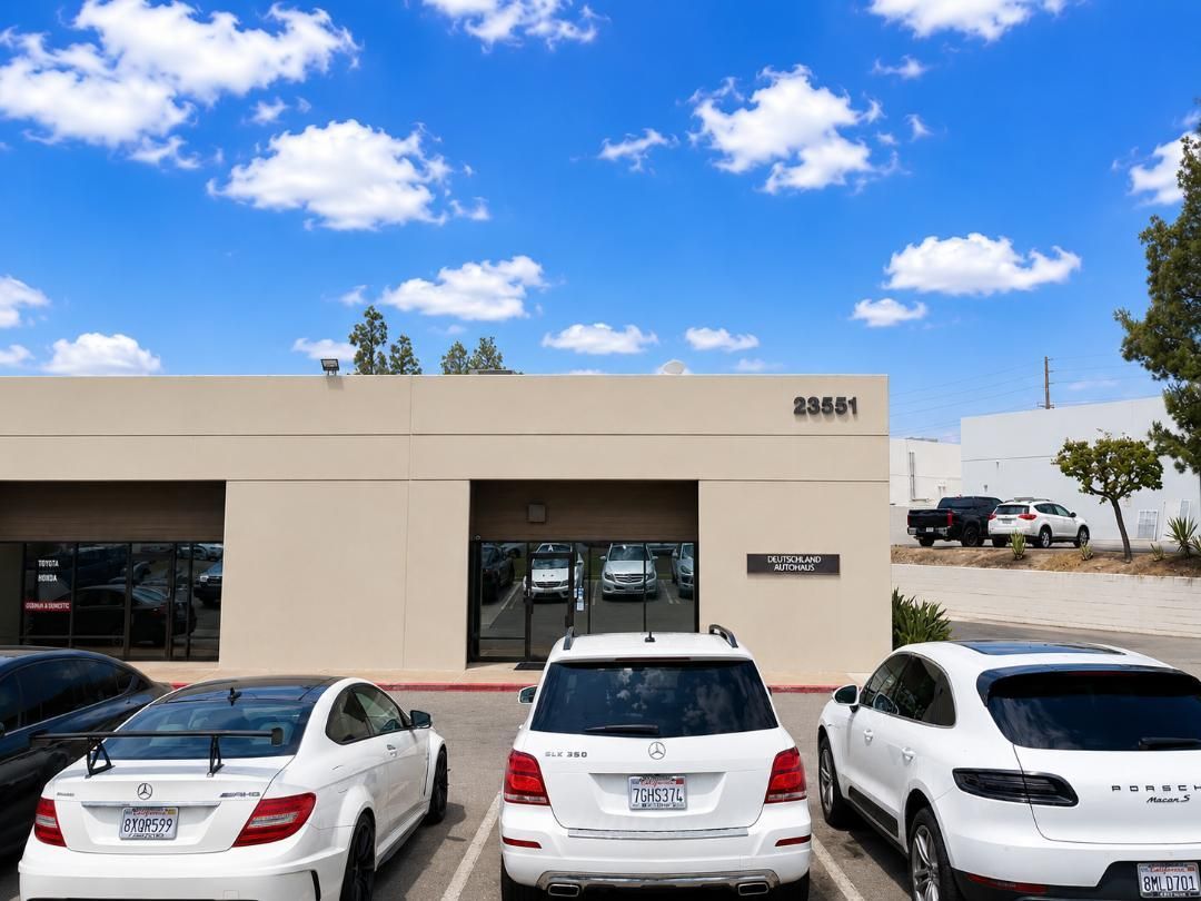 Parking lot with several cars in front of a beige commercial building under a blue sky.