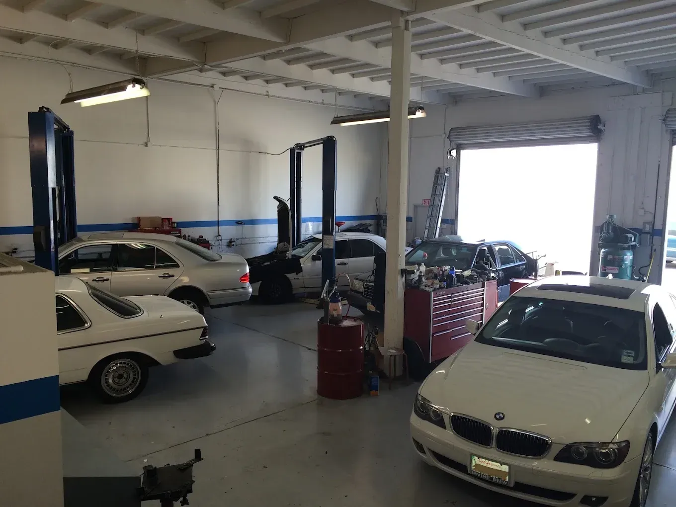 Auto repair shop with several cars on lifts and a white car in the foreground.