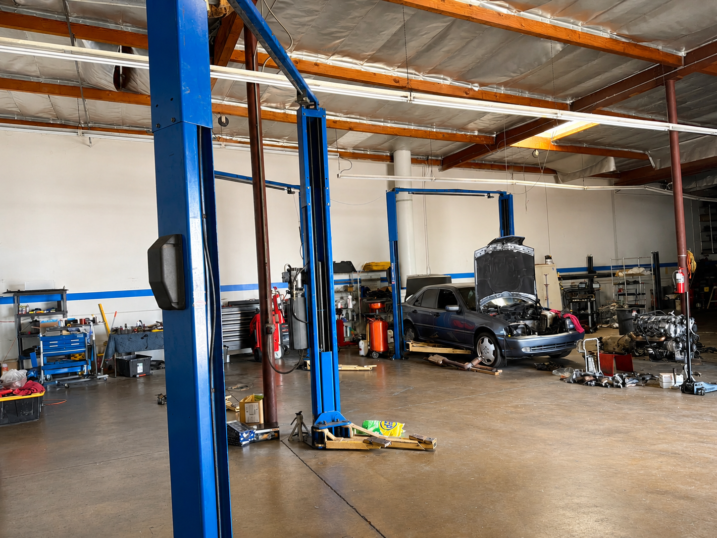 Auto repair shop with blue lifts, a raised car, and tools on a concrete floor.