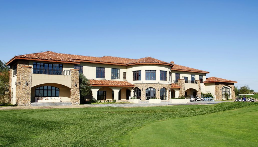 Large stone villa with a red tile roof and arched windows beside a green lawn under a clear blue sky