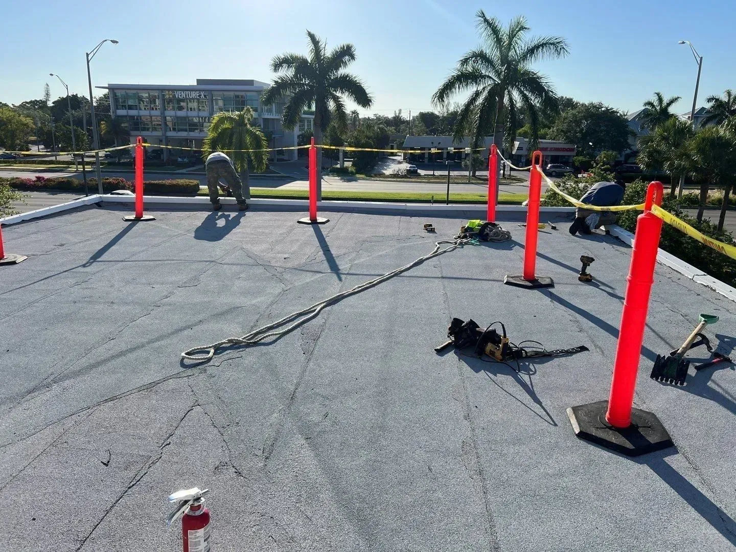 Outdoor obstacle course with red poles and ropes on a sunlit paved lot, with palm trees in the background