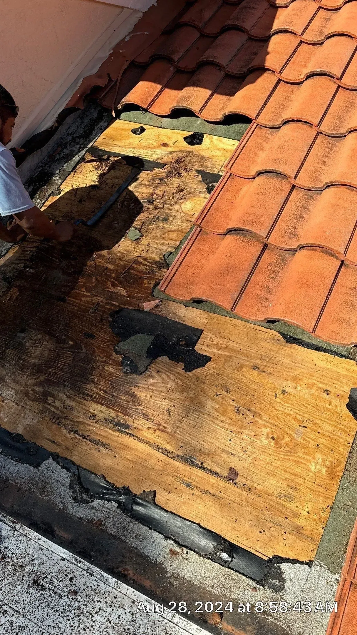 Damaged clay tile roof with black tar patches and water stains near the edge