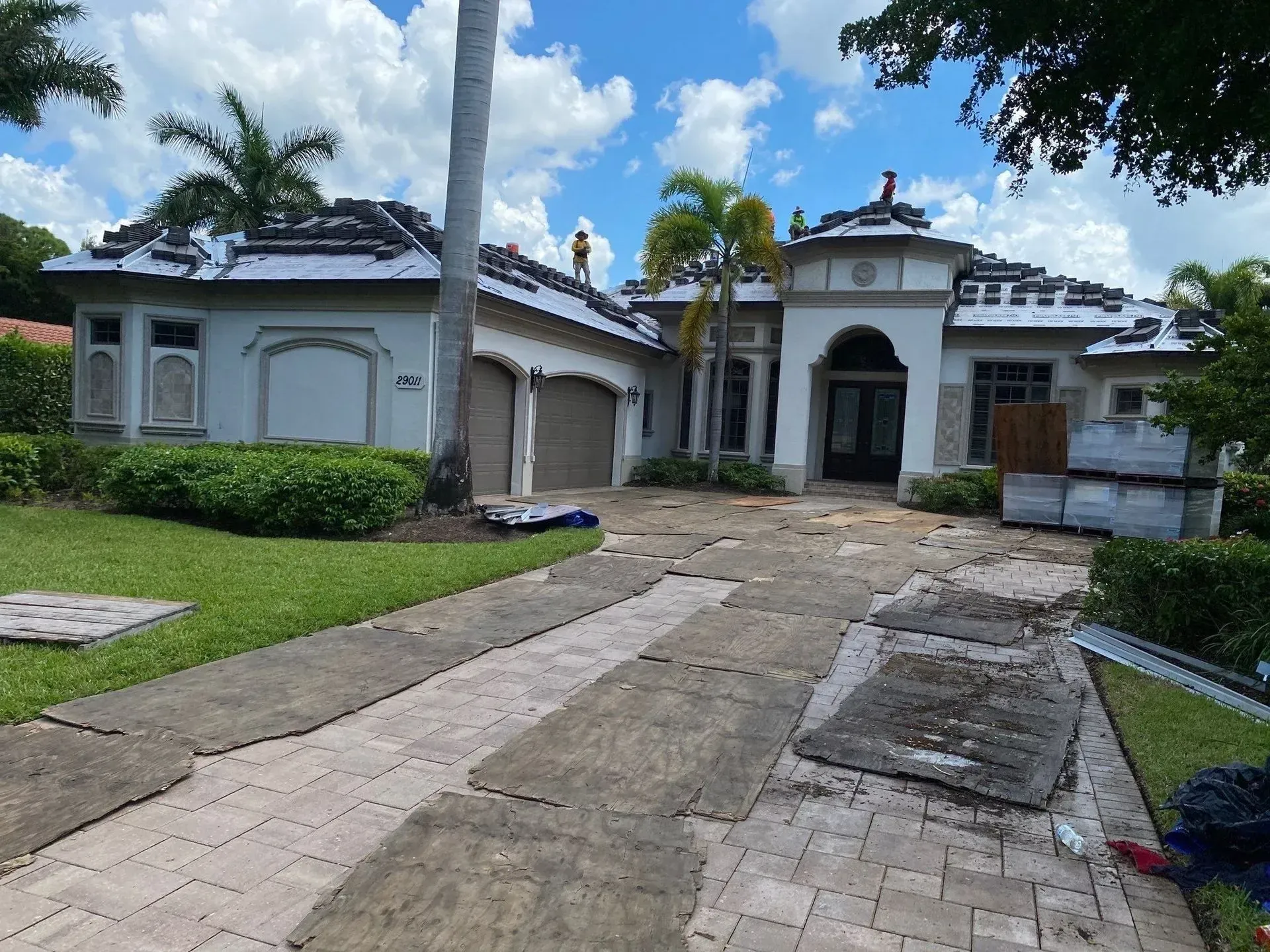White villa with a curved driveway, green lawn, and trees under a cloudy sky.